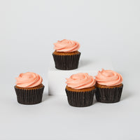 A box of four freshly baked cupcakes with peach-colored icing on top