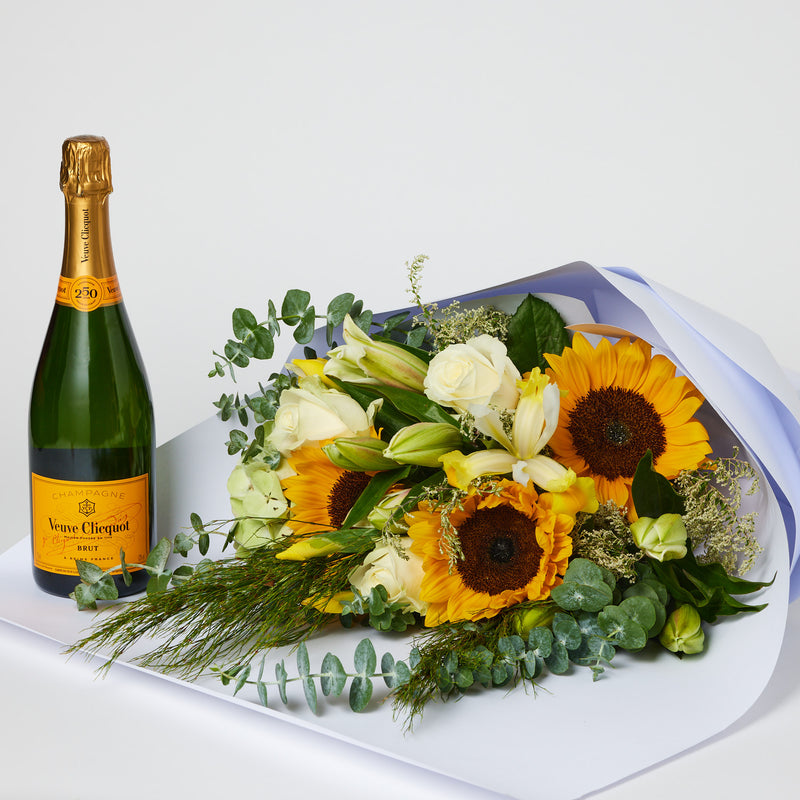Large honey toned flower bouquet wrapped in brown paper with satin ribbon and veuve clicquot champagne
