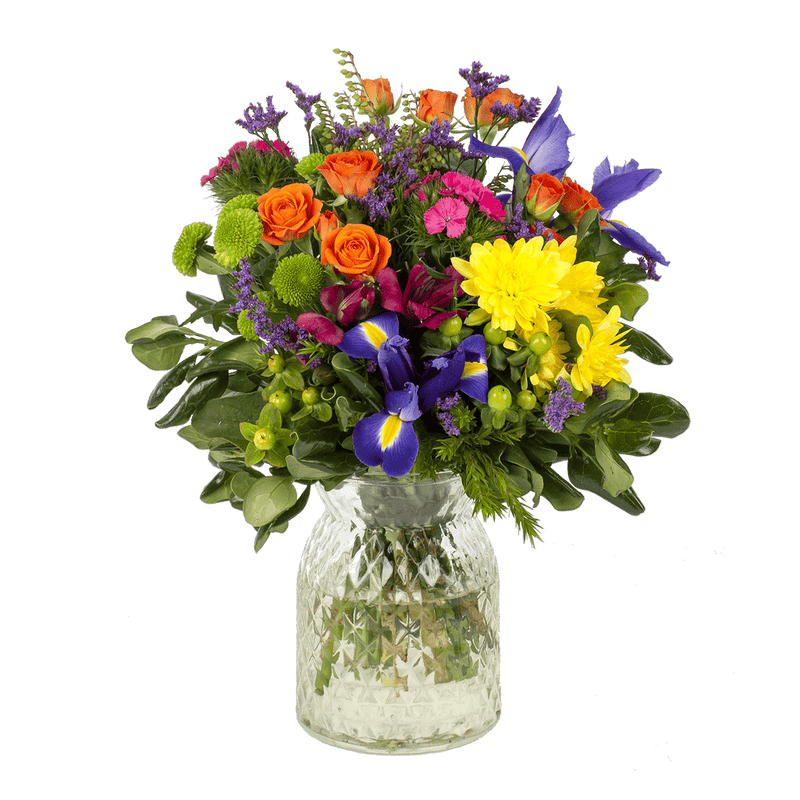 A vibrant seasonal posy of bright flowers and foliage in a clear glass vase.